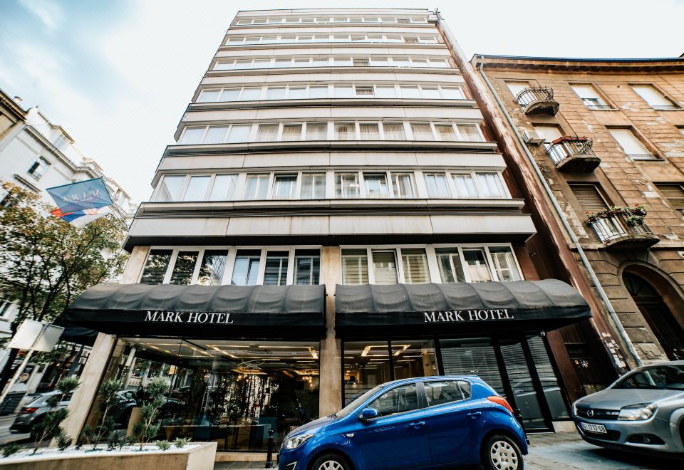 a brick building with a large parking lot in front of it , where a car is parked at Mark Hotel Belgrade