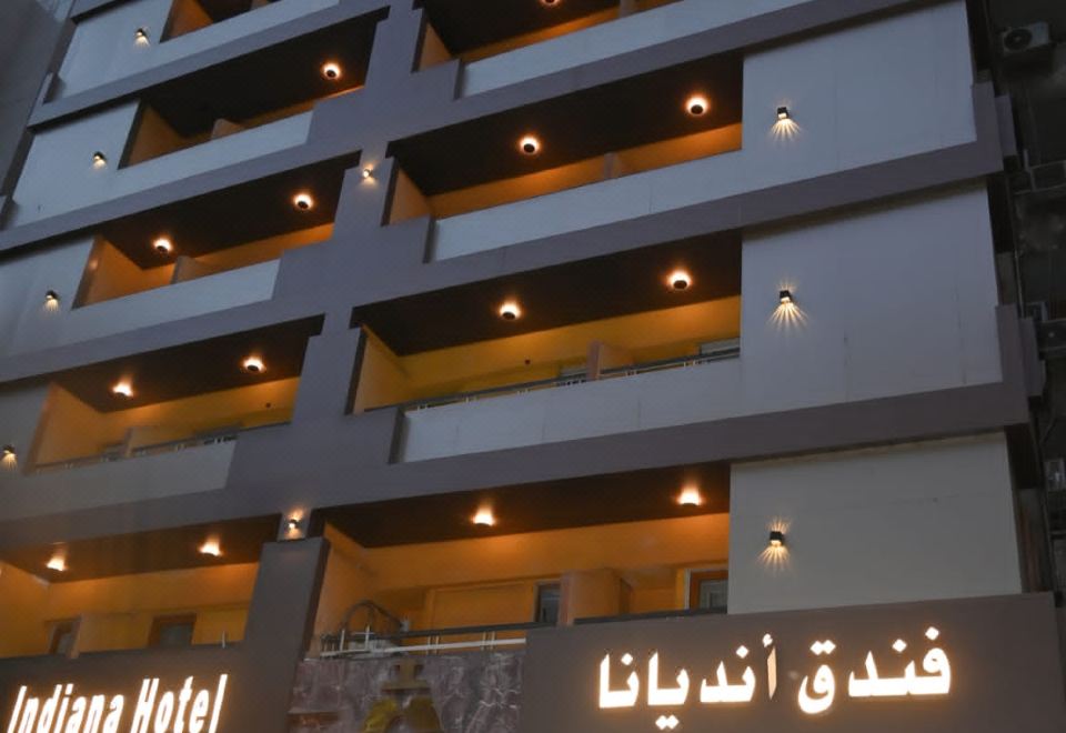 a modern hotel building with multiple floors and balconies , lit up at night against the backdrop of a city skyline at Indiana Hotel