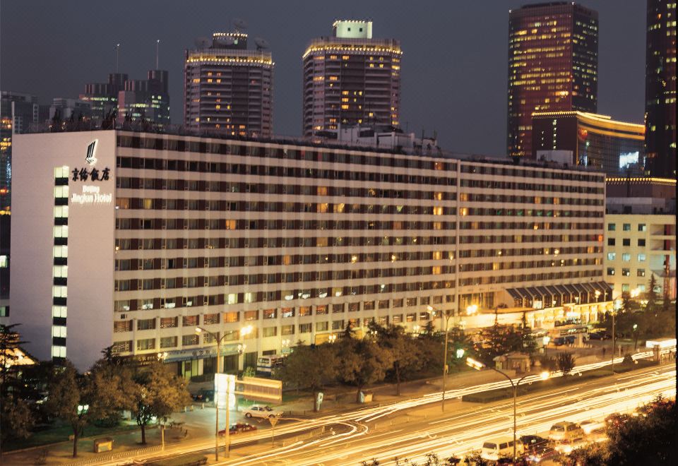 A large building with numerous windows is seen at dusk, during the twilight period at Jinglun Hotel