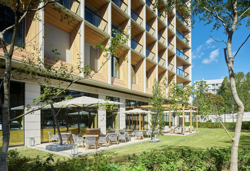 a modern building with large windows and a garden area with lounge chairs and umbrellas at Mitsui Garden Hotel Jingugaien Tokyo Premier