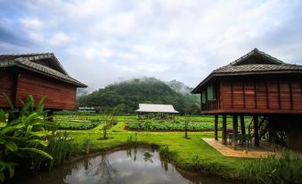 a serene garden with a pond , surrounded by wooden houses and lush greenery , under a cloudy sky at Lhongkhao Samoeng by Chi Villa