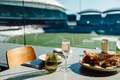 a dining table with a plate of food and a glass of champagne placed on it at Oval Hotel at Adelaide Oval, an EVT hotel