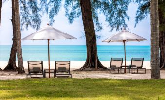 a tropical beach scene with umbrellas , chairs , and tables under a clear blue sky , overlooking the ocean at Outrigger Khao Lak Beach Resort