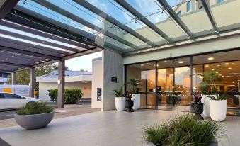 a modern building with a glass roof , surrounded by plants and potted trees , under a clear blue sky at Sudima Auckland Airport