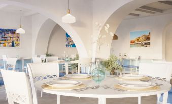 a modern restaurant with white tables and chairs , blue vases , and white arches , under a bright blue light at Iberostar Selection Creta Marine