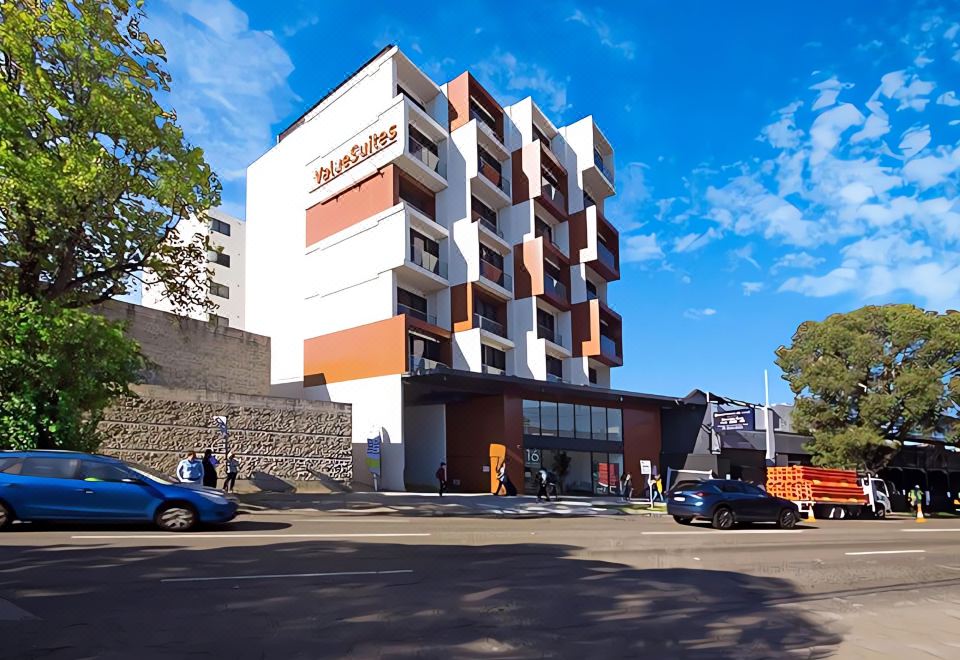 a large white building with orange accents , situated on a street corner with cars parked in front at ValueSuites Green Square