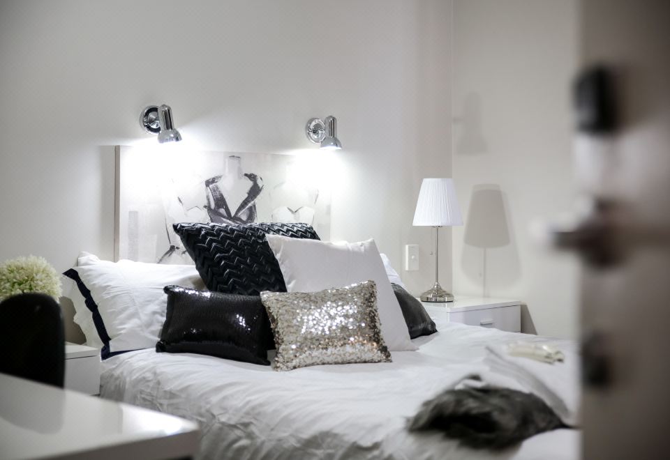 a white bedroom with a bed adorned with black and white pillows , creating a clean and elegant atmosphere at Airport Hotel Sydney