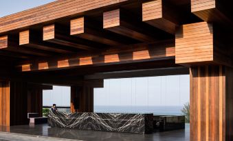 a wooden structure with a stone counter and a person standing near the entrance , overlooking the ocean at The Naka Phuket, a member of Design Hotels