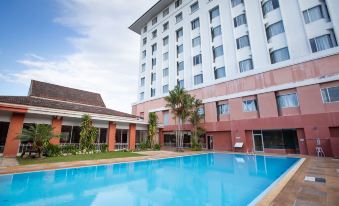 a large swimming pool is surrounded by a hotel building with palm trees and red fencing at The Imperial Narathiwat Hotel