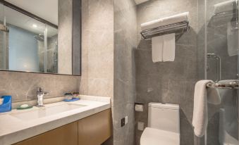 The bathroom in this hotel room includes a toilet, sink, and a large mirror mounted on the wall above the shower stall at Jinfan Wanyuan Hotel