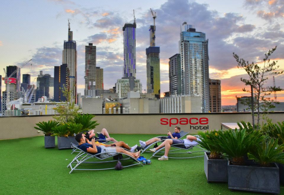 "a group of people relaxing on lounge chairs in a city setting , with a sign for "" space hotel "" visible in the background" at Space Hotel