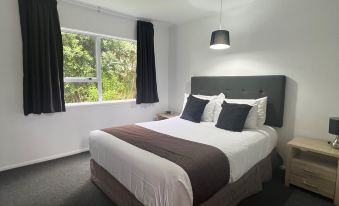a bedroom with a large bed , black curtains , and a window with a view of trees at Asure Green Gables Motel