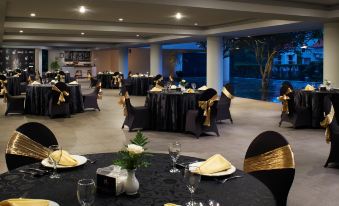 a large dining room with multiple tables set for a formal event , including black tablecloths , chairs , and vases filled with flowers at El Hotel Malang