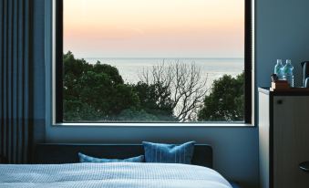 a bed with blue pillows is positioned in front of a window that overlooks the ocean and trees at Fairfield by Marriott Mie Kumano Kodo Mihama