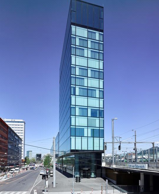 a tall , modern building with a glass exterior is situated on a street corner near other buildings and under a clear blue sky at Arte Hotel Salzburg