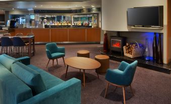 a modern lounge area with blue chairs and a wooden coffee table , featuring a fireplace and a bar at DoubleTree by Hilton Manchester Airport