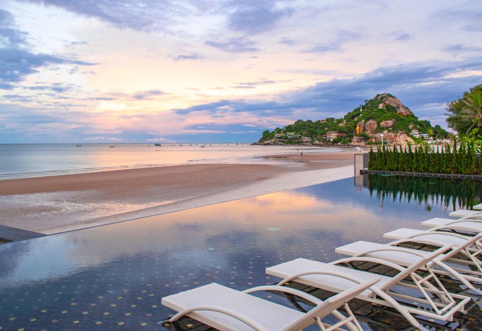 a serene beach scene with white lounge chairs lining the edge of a pool , creating a relaxing atmosphere at The Yana Villas Hua Hin