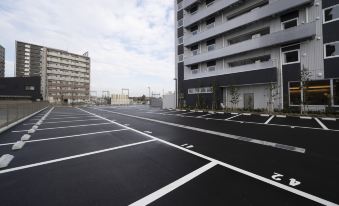 an empty parking lot with a black and white striped road , surrounded by buildings and trees at Just Inn Matsusaka Station