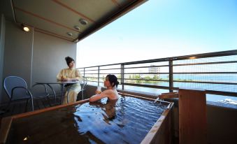 a woman is soaking in a hot tub on a balcony , while another person looks on at Biwako Ryokusuitei