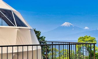 The balcony offers a picturesque view of mountains, the ocean, and a clear blue sky at Nishi-izu Glamping Tenkuu-Terrace