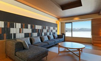 a modern living room with a gray sectional couch , wooden coffee table , and large window overlooking a lake at Lake Akan Tsuruga Wings
