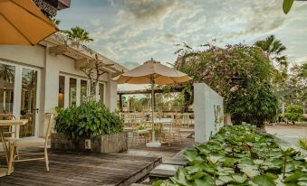 an outdoor dining area with a wooden table , chairs , and umbrellas , surrounded by lush greenery at Pelangi Beach Resort & Spa, Langkawi