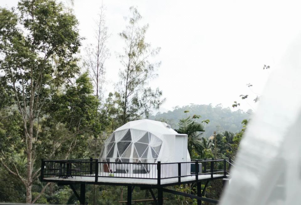 a white geodesic dome tent is perched on a wooden platform with a railing , overlooking a forested area at Khaopubpa Resort