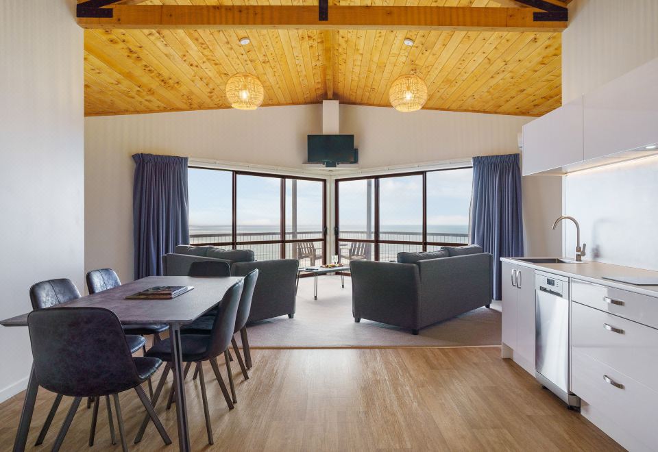 a modern living room with wooden ceiling , blue curtains , and large windows offering views of the ocean at Castaways Resort