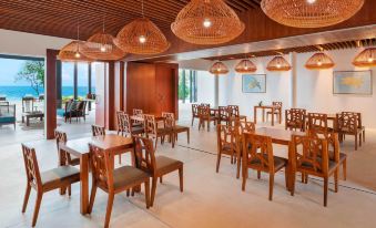 a large dining room with wooden chairs and tables , surrounded by windows overlooking the ocean at The Westin Maldives Miriandhoo Resort