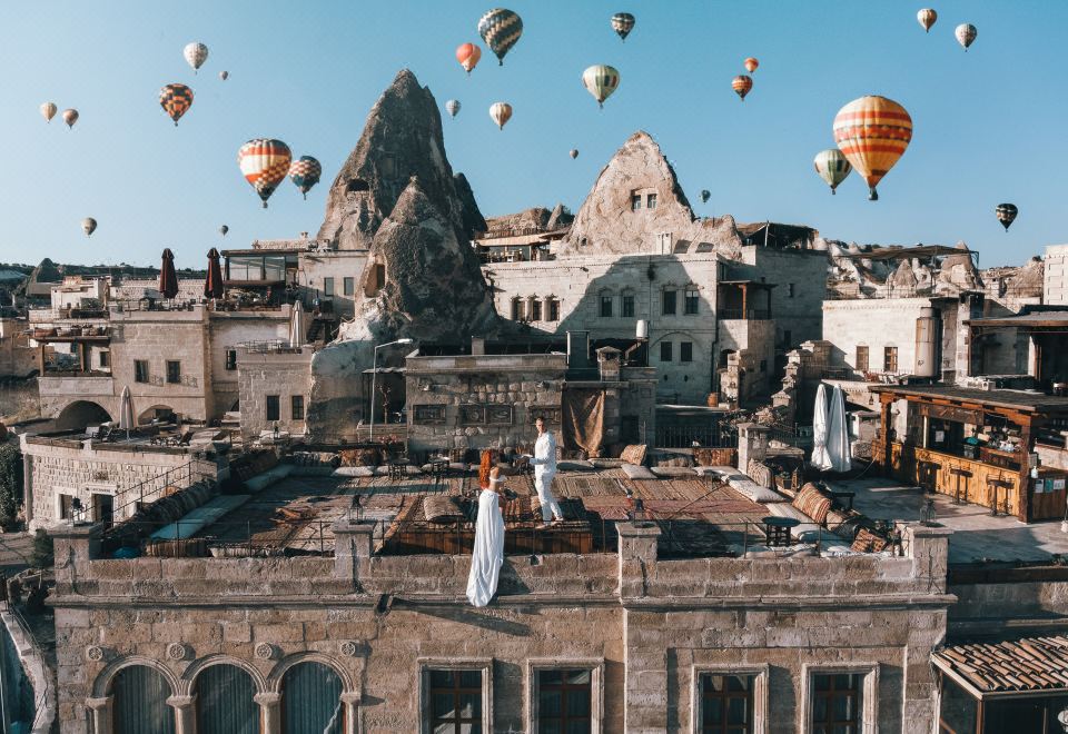 a large group of hot air balloons floating in the sky above an old building , with people and buildings in the background at Sultan Cave Suites