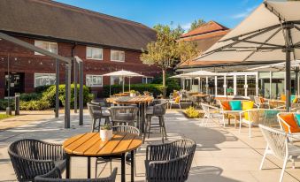 an outdoor dining area with several tables and chairs , as well as umbrellas for shade at Holiday Inn Aylesbury