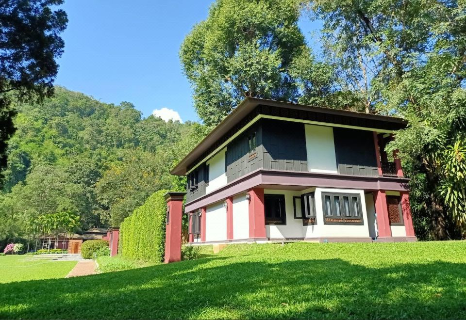 a house with a red roof and white walls is surrounded by green grass and trees at Lanna Resort Chiang Mai