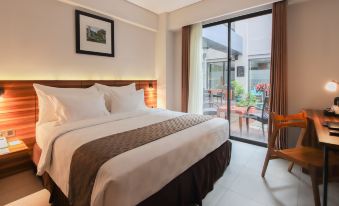 a large bed with white linens is in a room with a sliding glass door leading to an outdoor patio at Swiss-Belinn Timika
