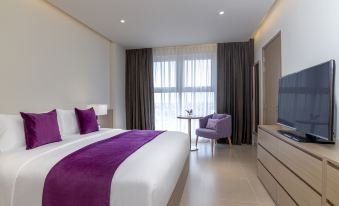 a modern bedroom with a white bed , purple bedding , and a large window overlooking the city at Mercure Hai Phong