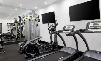 a well - equipped gym with various exercise equipment , including treadmills and weight machines , in a white - walled room at ValueSuites Green Square