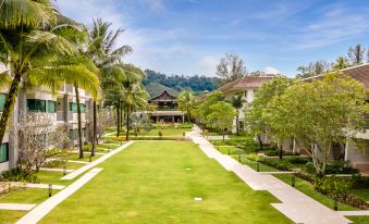 a lush green lawn surrounded by palm trees , with a house in the background , under a clear blue sky at Outrigger Khao Lak Beach Resort