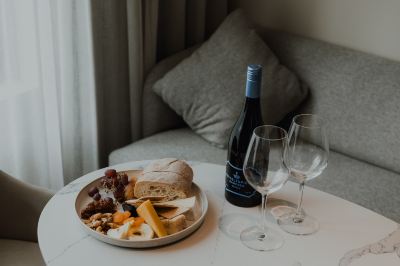 a table with a plate of bread , cheese , nuts , and a bottle of wine is set up in front of a couch at Oval Hotel at Adelaide Oval, an EVT hotel