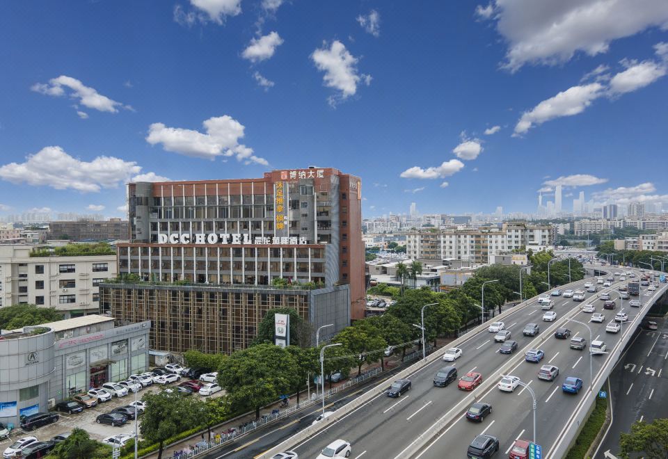 A large building with numerous windows and cars on the street in front, set against a city backdrop at DCC Hotel (Guangzhou Tianhe Coach Terminal Station)