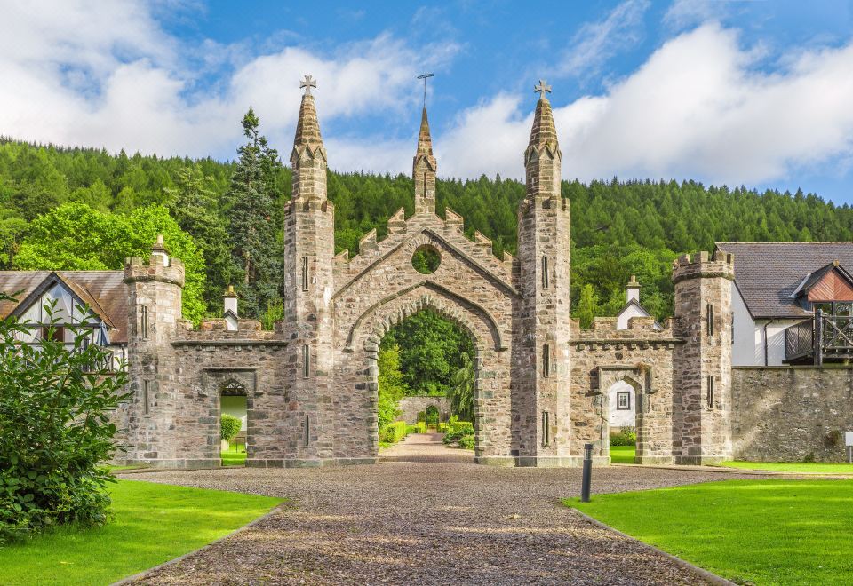 a large stone archway with spires and a circular center is surrounded by trees and a path at The Kenmore Club