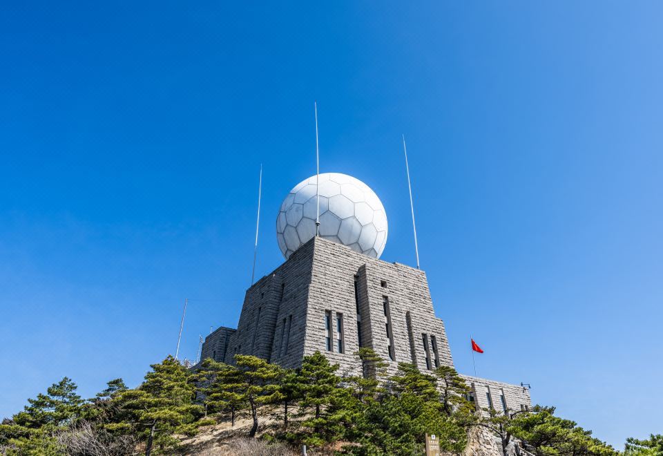 a picturesque scene featuring a tall stone tower set against a backdrop of trees and a clear blue sky at Guangmingding Hotel