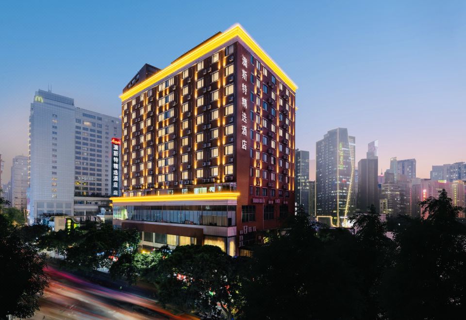 A well-lit, large building with numerous windows and an adjacent hotel in the center creates a stunning and lively ambiance at night at Guangzhou Zhujiang New Town Ausotel Smart Hotel, Canton Fair Free Shuttle