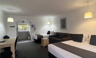 a hotel room with a large bed , couch , and dining table , all set up in a well - lit living area at Asure Green Gables Motel
