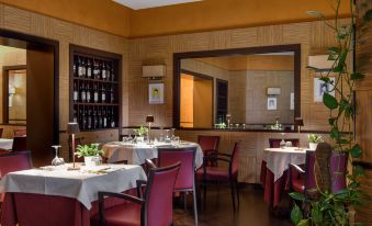 a dining room with red chairs and tables , a mirror on the wall , and wine bottles in the background at Grand Hotel Adriatico