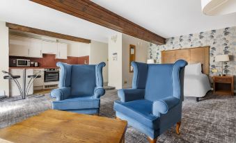 two blue armchairs are placed in a room with a wooden table and a kitchen visible through the window at Thurnham Hall