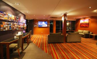 a modern , well - lit room with a large screen tv , couches , and tables , as well as a bookshelf filled with books at Stay at Alice Springs Hotel