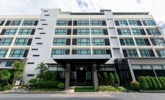 a modern building with a white facade and large windows , featuring a black door and a potted plant on the sidewalk at Grand Ratchapruek Hotel