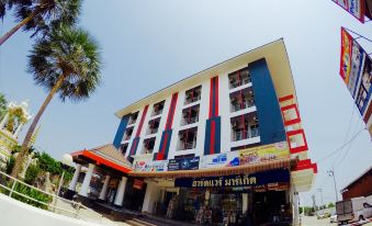 a large building with a red and white facade , located in a city setting with palm trees at Thanarom Place