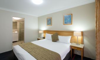 a large bed with a wooden headboard and white linens is in a room with a painting on the wall at APX Parramatta