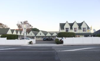 a row of green - colored houses with white walls and trees , standing in front of a clear blue sky at Asure Green Gables Motel