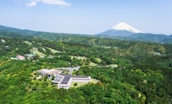a lush green valley with a snow - capped mountain in the background and a large building surrounded by trees at Izu Marriott Hotel Shuzenji